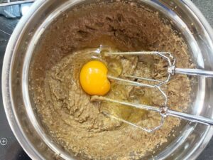 An egg added to peanut butter and sweetener in a mixing bowl.