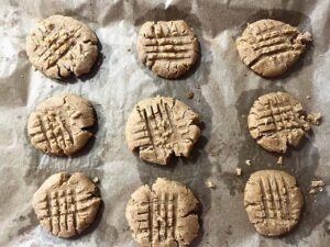 Oat Flour Peanut Butter Cookies pressed with a fork and laying on a parchment-lined baking pan.