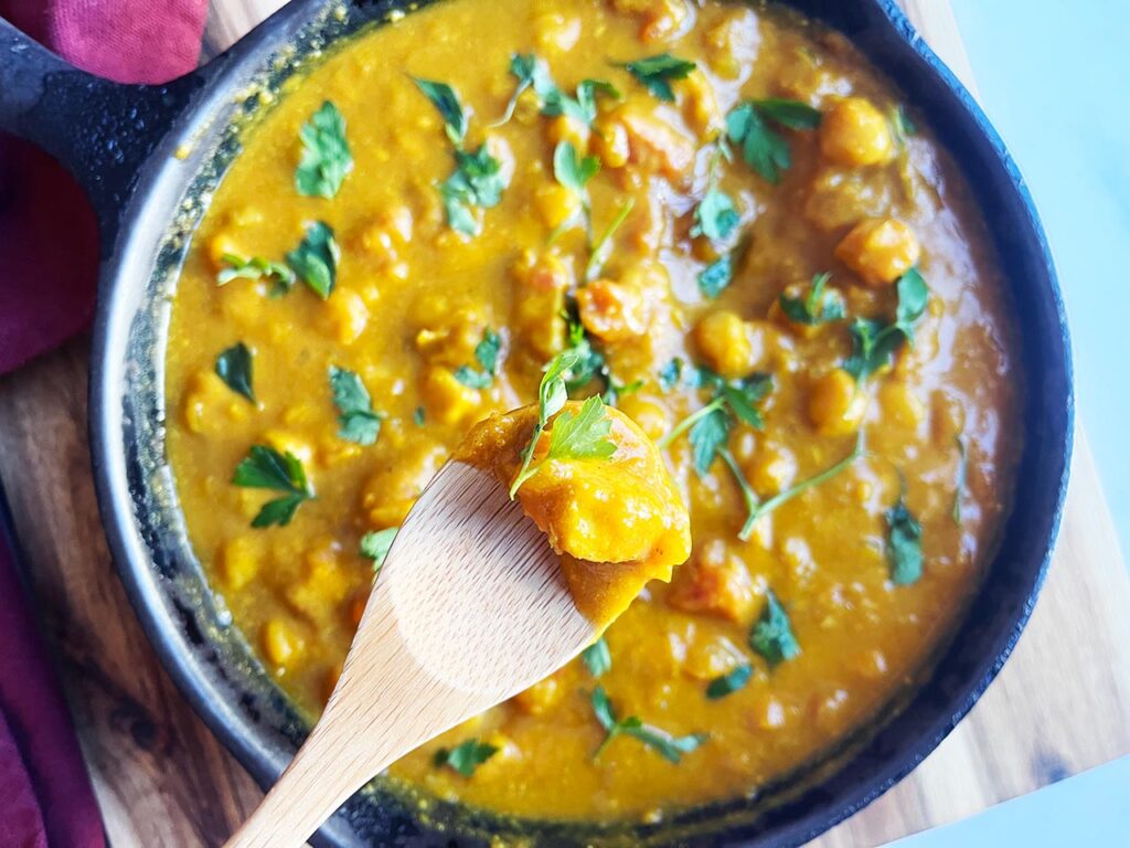 Overhead view of a spoon lifting up some Pumpkin Curry from a skillet.