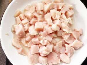 Chicken breasts cut into small pieces, on a white plate.