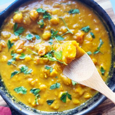 Overhead focus. A wood spoon lifts up a bite of Pumpkin Curry from a skilet.