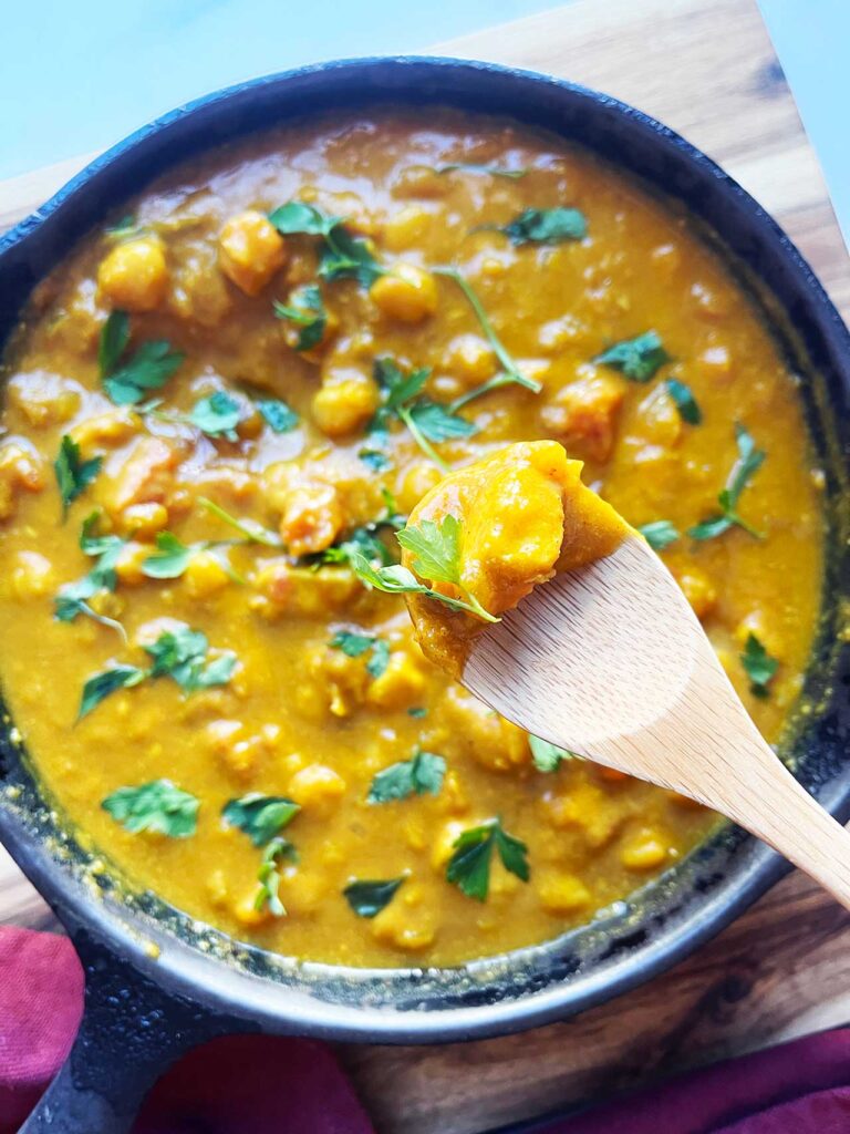 Overhead focus. A wood spoon lifts up a bite of Pumpkin Curry from a skilet.