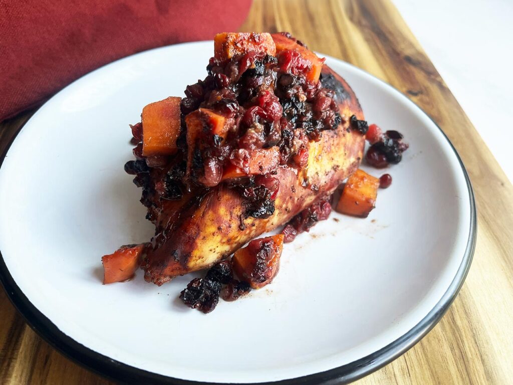 A white plate withSheet Pan Cranberry Chicken, sitting on a wood surface.