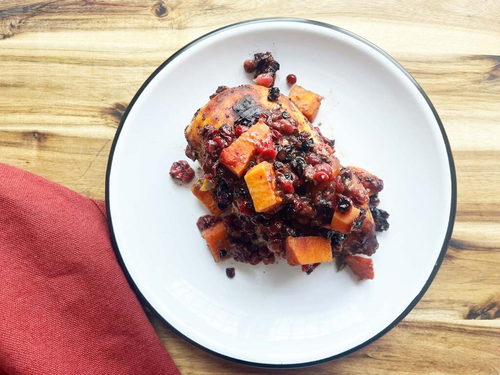 Overhead focus. Sheet Pan Cranberry Chicken on a white plate, sitting on a wood surface.