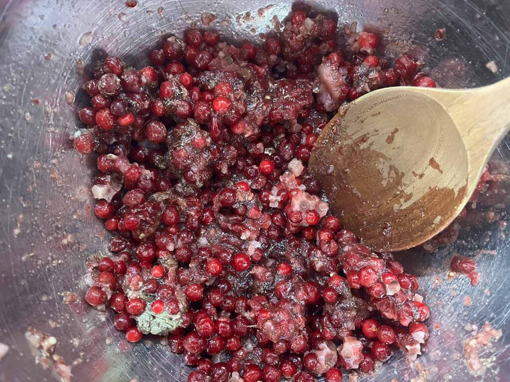 Frozen cranberries mixed with sauce ingredients in a mixing bowl.