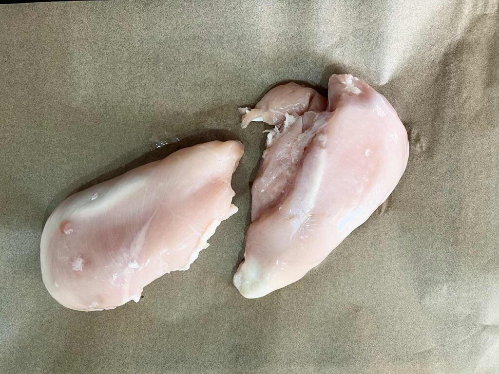 Two chicken breasts on a parchment-lined sheet pan.