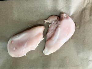 Two chicken breasts on a parchment-lined sheet pan.