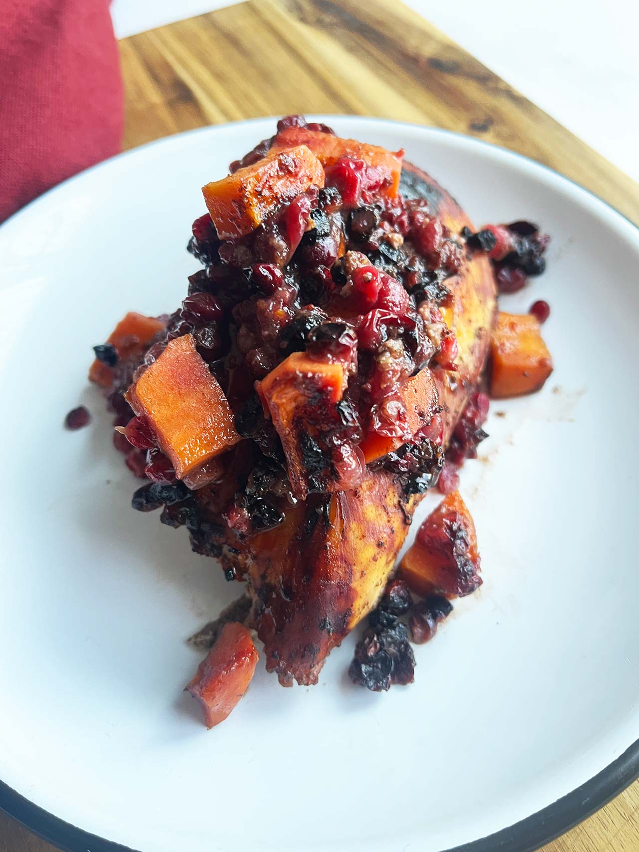 A Sheet Pan Cranberry Chicken breast on a white plate covered in cranberry sauce and sweet potatoes.