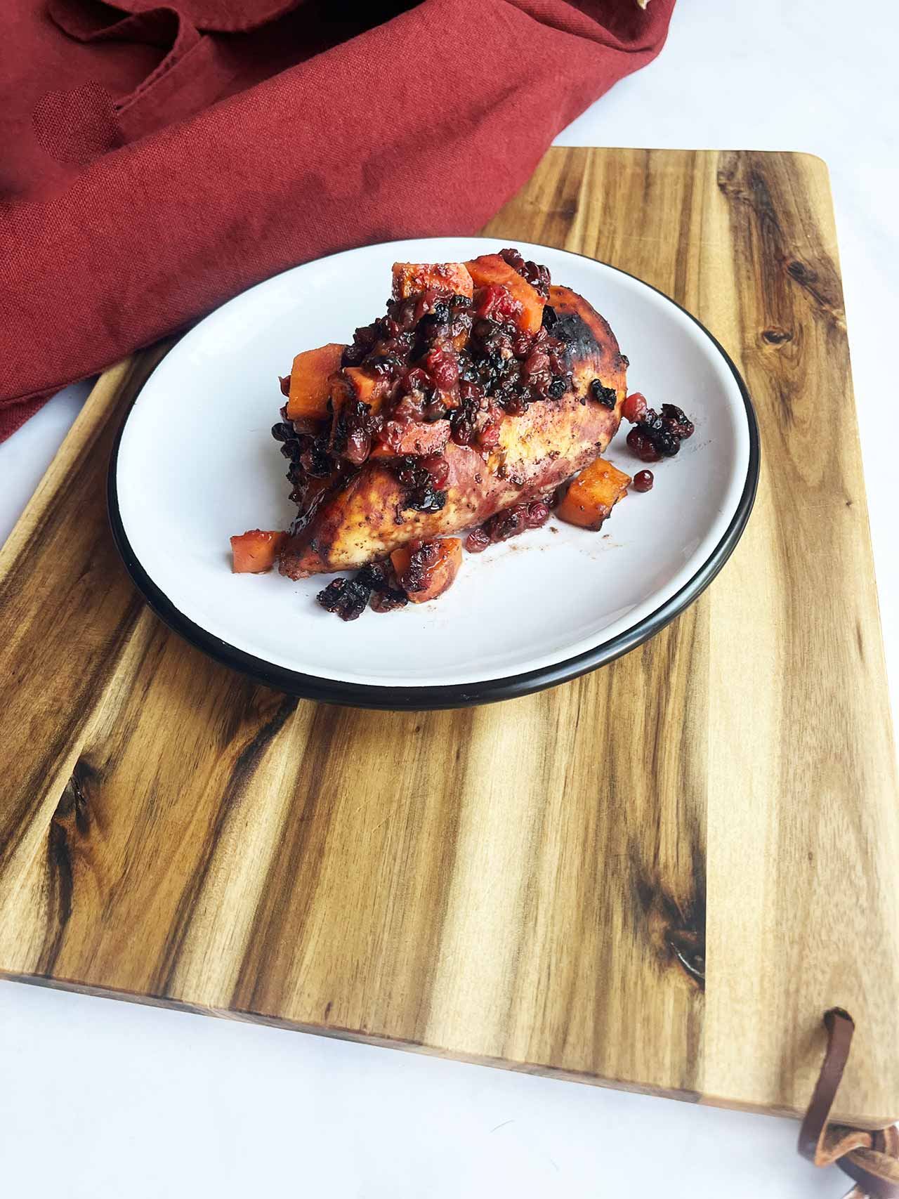 Angled view. A white plate with a serving of Sheet Pan Cranberry Chicken sitting on a wood cutting board.