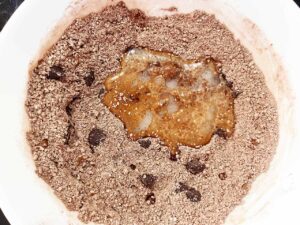 Wet ingredients added to dry ingredients for a single chocolate cookie in a mixing bowl.