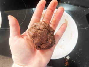 Cookie dough for a single chocolate cookie rolled into a ball, held in a hand.