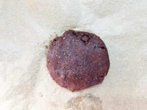 Cookie dough flattened into a round cookie and set on a parchment-lined cookie sheet.