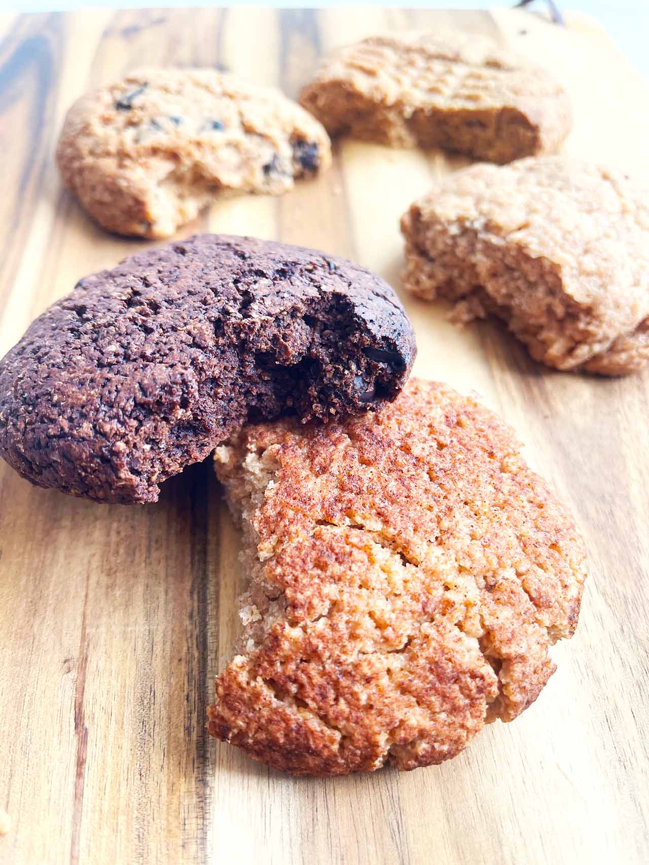 Different cookies scattered over a wood cutting board.