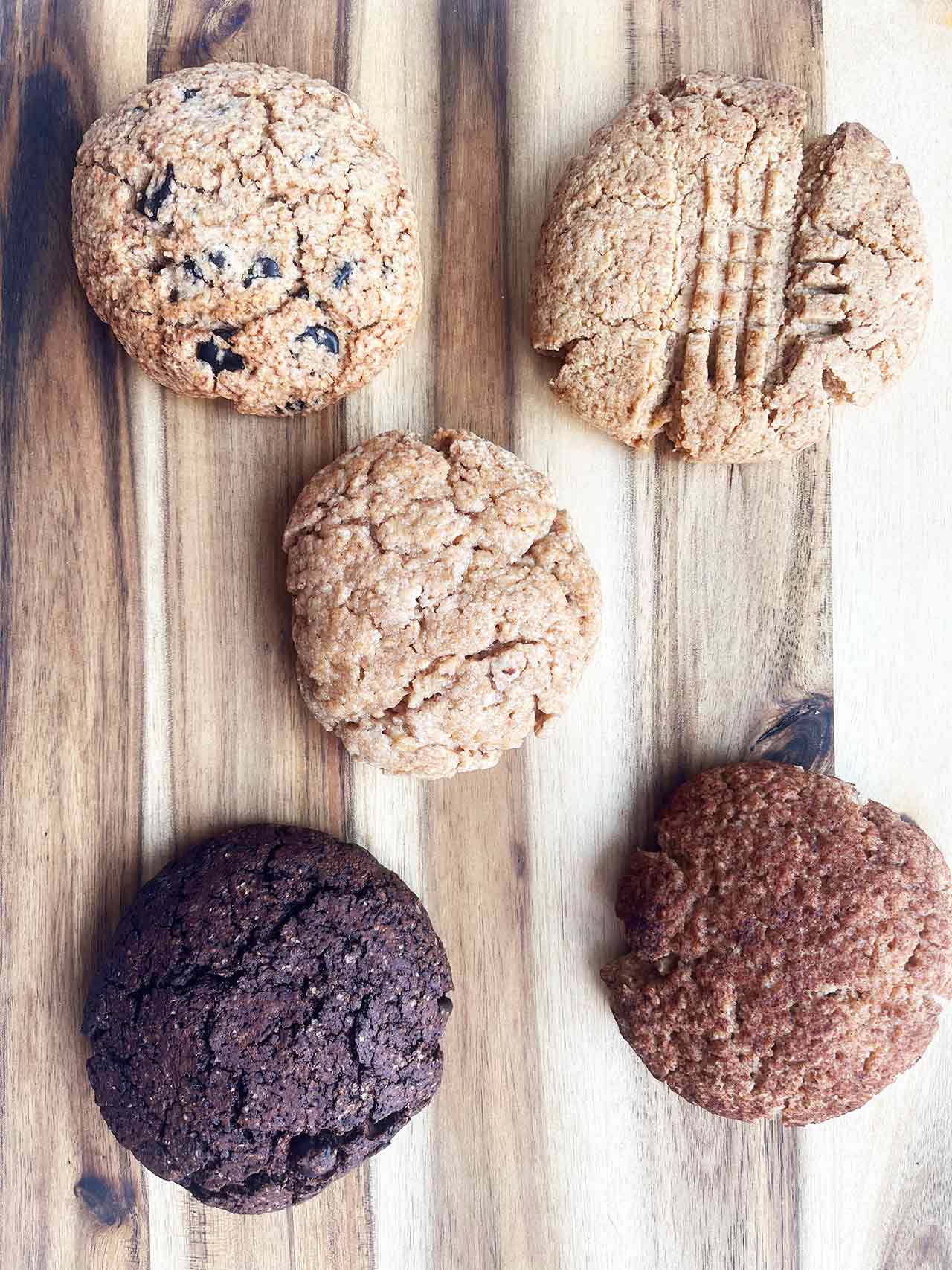Overhead focus. Five different whole cookies arranged on a wood cutting board.
