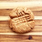 A baked, single peanut butter cookie on a wood surface.