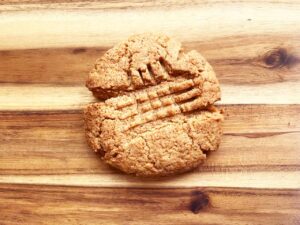 A baked, single peanut butter cookie on a wood surface.