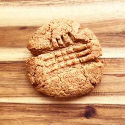 A baked, single peanut butter cookie on a wood surface.
