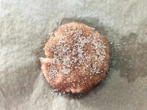 A snickerdoodle flattened and placed on a parchment-lined cookie sheet and sprinkled with extra cinnamon sugar.
