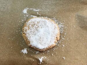 Sugar cookie dough ball, flattened and sprinkled with extra sweetener on a parchment-lined cookie sheet.