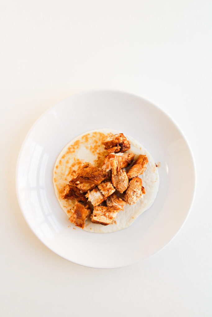 Building the Street Corn Chicken Tacos with a layer of chicken on a tortilla.