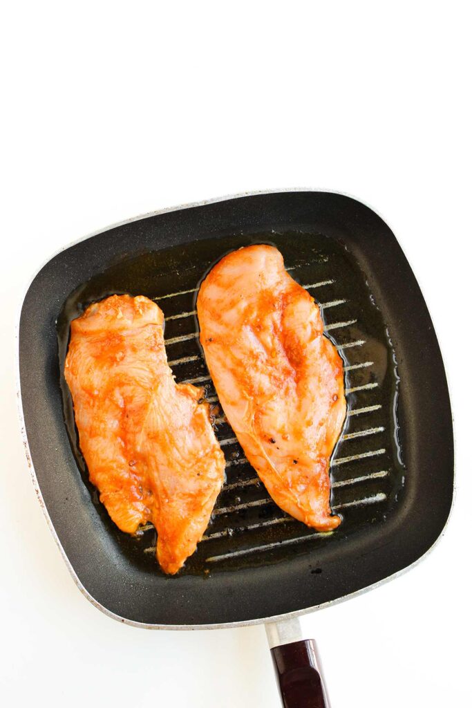 Cooking chicken breasts with sauce in a skillet.