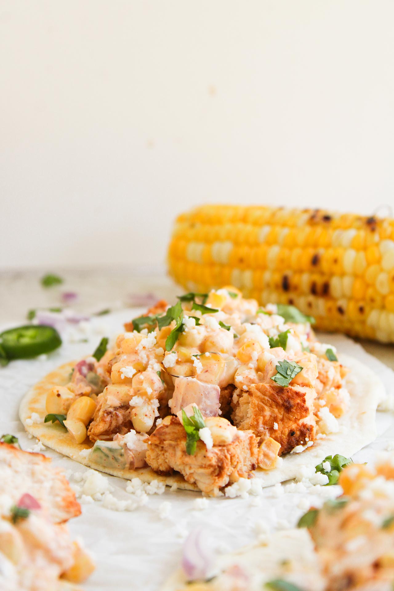 Selective focus. A single Street Corn Chicken Taco in front of a charred cob of corn.