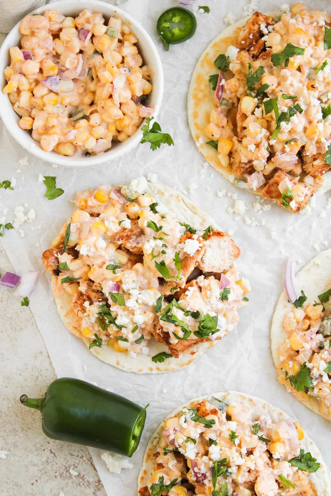 Overhead focus. Multiple Street Corn Chicken Tacos and a bowl of corn mix on a piece of parchment.