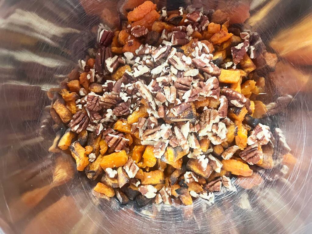 Pecans added to sweet potatoes in a mixing bowl.