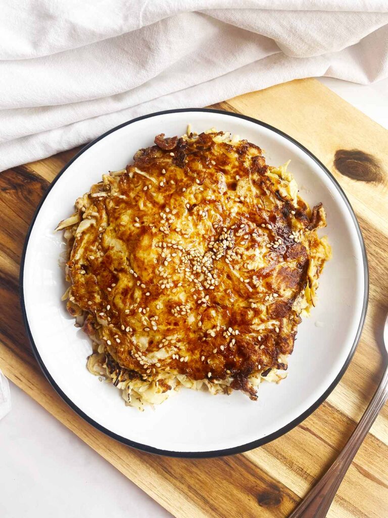 Overhead focus. Cabbage Pancakes on a white plate sitting on a wood cutting board with a spoon and white towel.