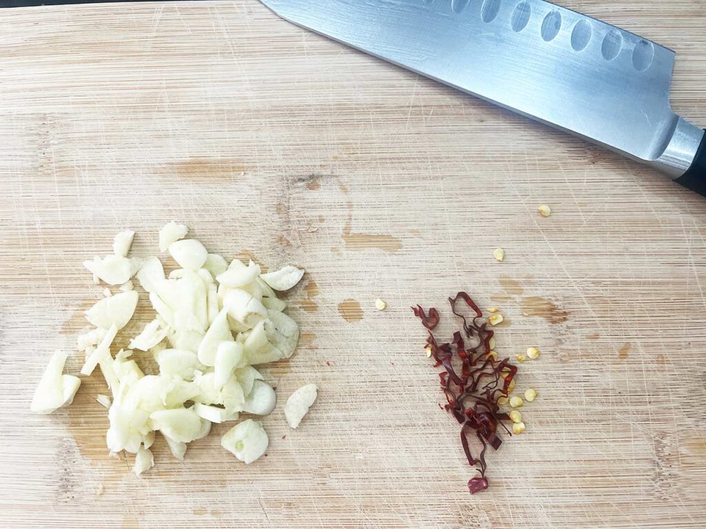 Sliced garlic and red chili pepper on a cutting board with a knife.