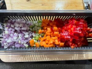 Chopped vegetables in a chopper. Onions, celery, carrots, and a red bell pepper.