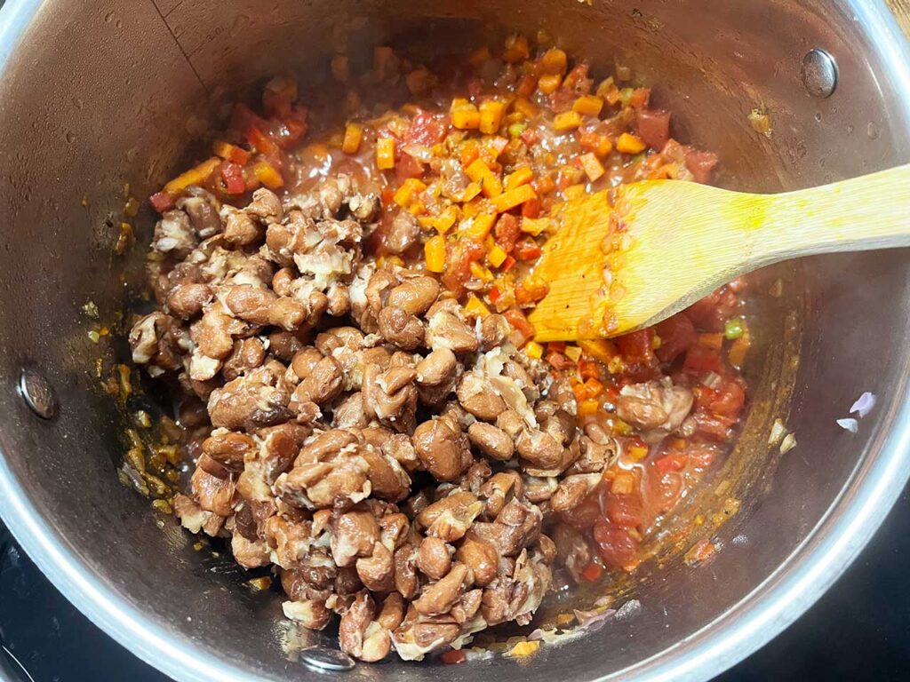 Cooked pinto beans added to a soup pot.