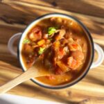 Overhead focus. A small wood spoon lifts some Mexican Pinto Bean Soup out of a full bowl.