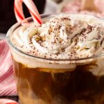 Partial front view of a glass mug filled with Peppermint Latte and holding a candy cane.