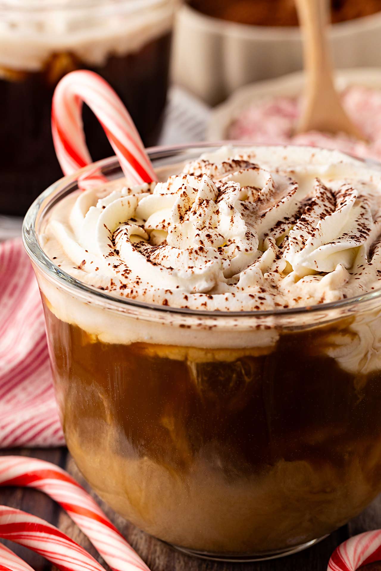 Partial front view of a glass mug filled with Peppermint Latte and holding a candy cane.