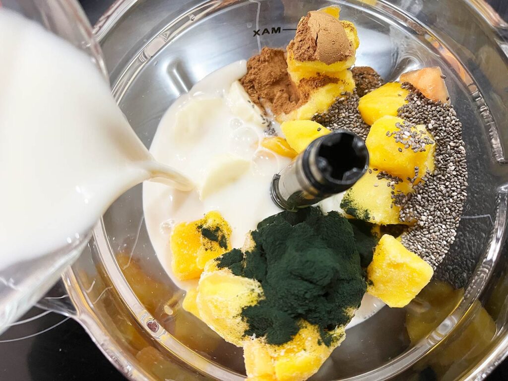 Spirulina Smoothie Recipe ingredients in a blender as milk is being poured in.