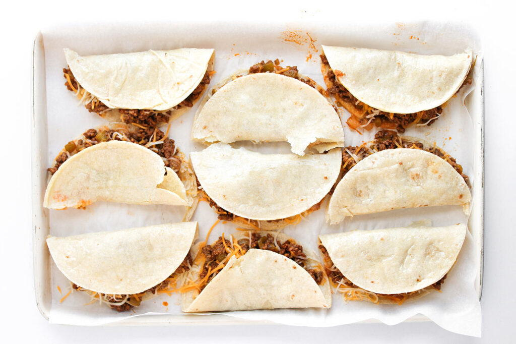 Stuffed Baked Beef Tacos ready for the oven on a parchment-lined baking sheet.