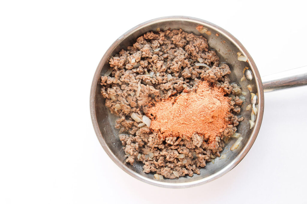 Adding taco seasoning to meat in a skillet.