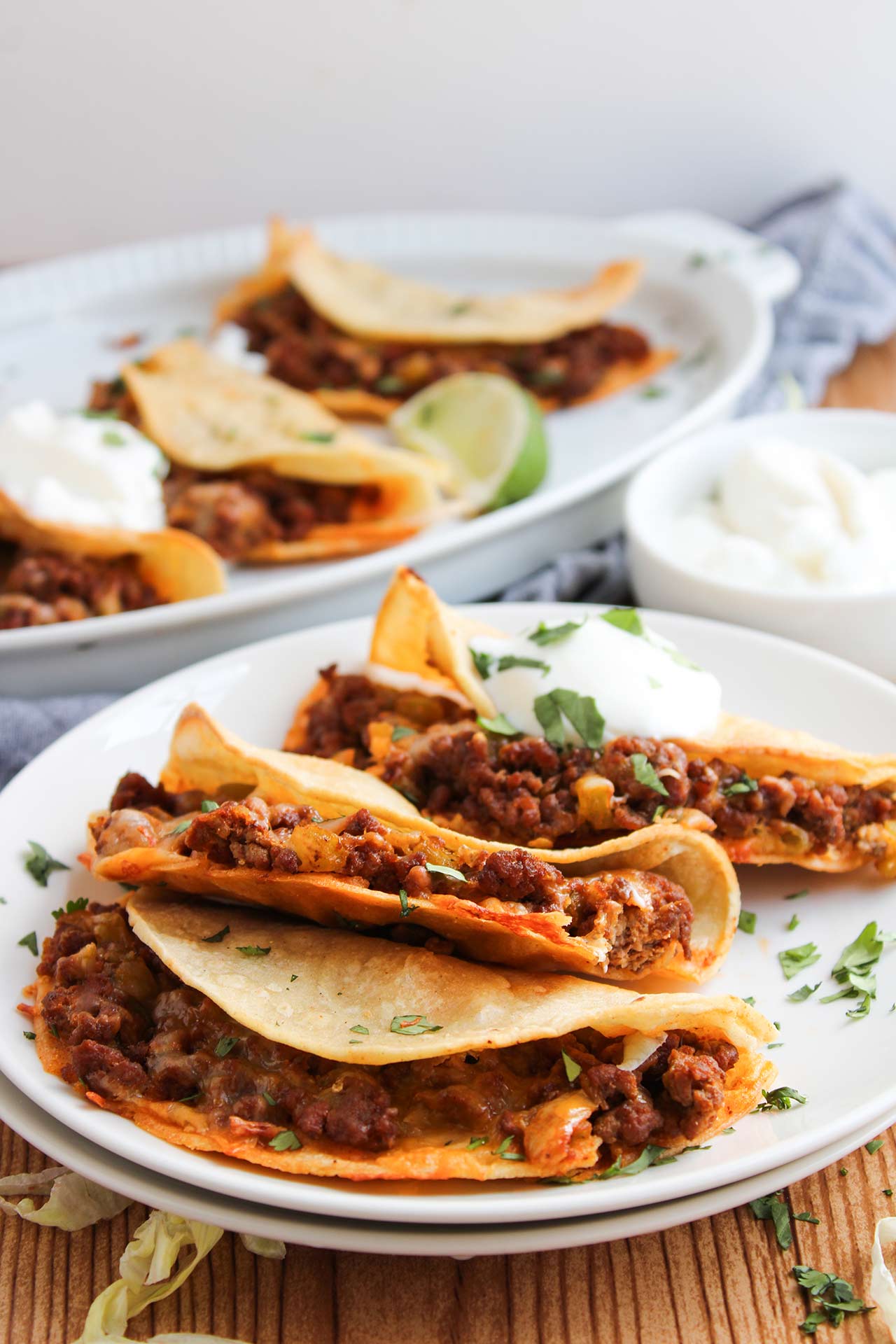 Front focus. A white plate with three Baked Beef Tacos, sitting next to a serving platter of the same.