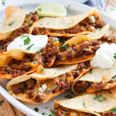 Close up front focus. A white platter holds many Baked Beef Tacos.