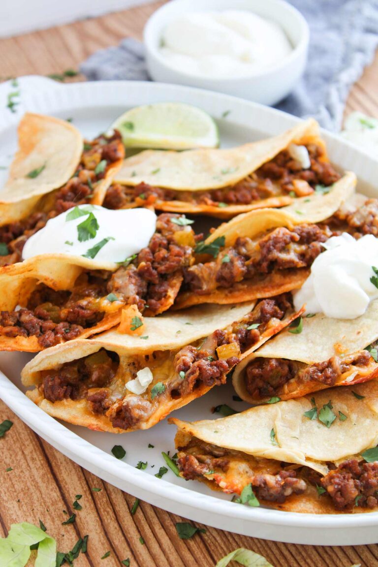 Close up front focus. A white platter holds many Baked Beef Tacos.