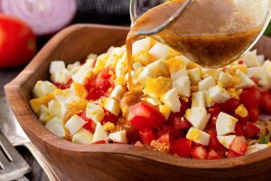 Pouring dressing over a High Protein Dense Bean Salad in a wood bowl.
