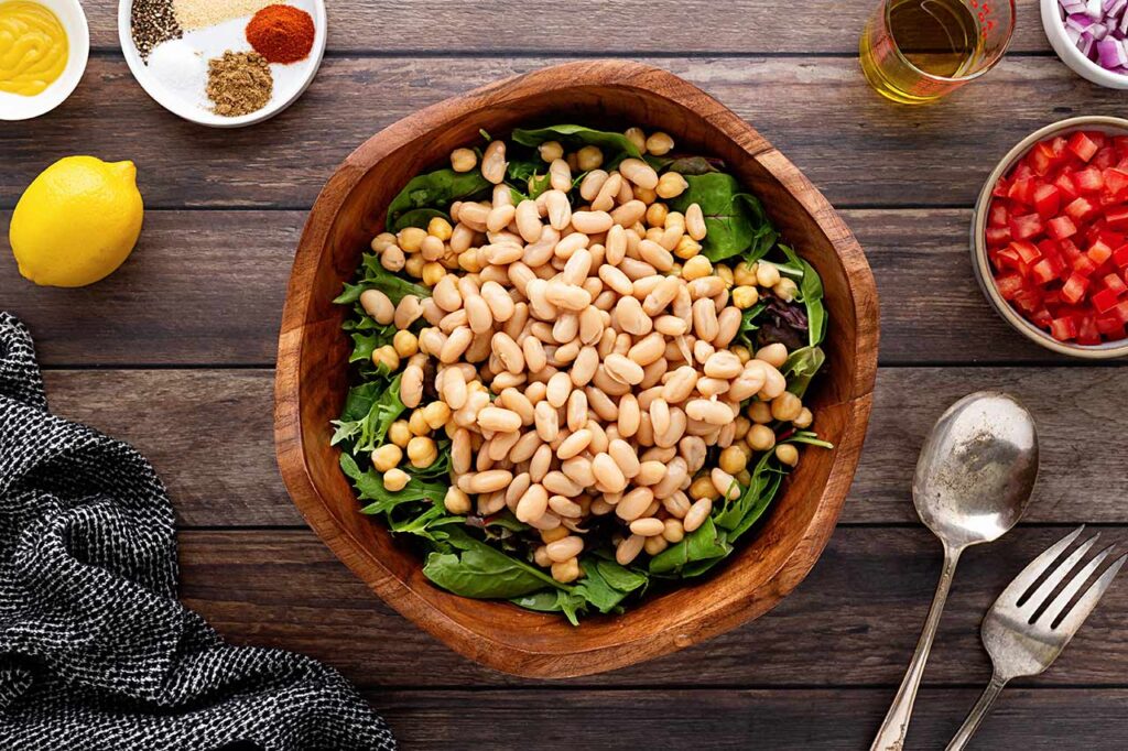 A layer of beans over lettuce in a wood bowl.