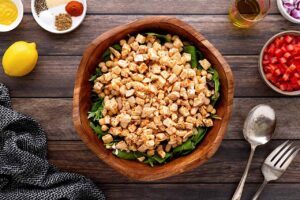 Chopped chicken over beans and lettuce in a wood bowl.