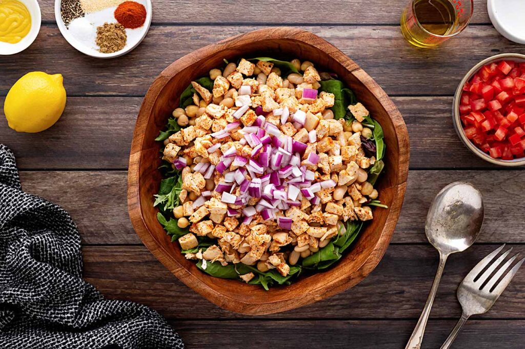 Raw, chopped onions added to salad layers in a wood bowl.