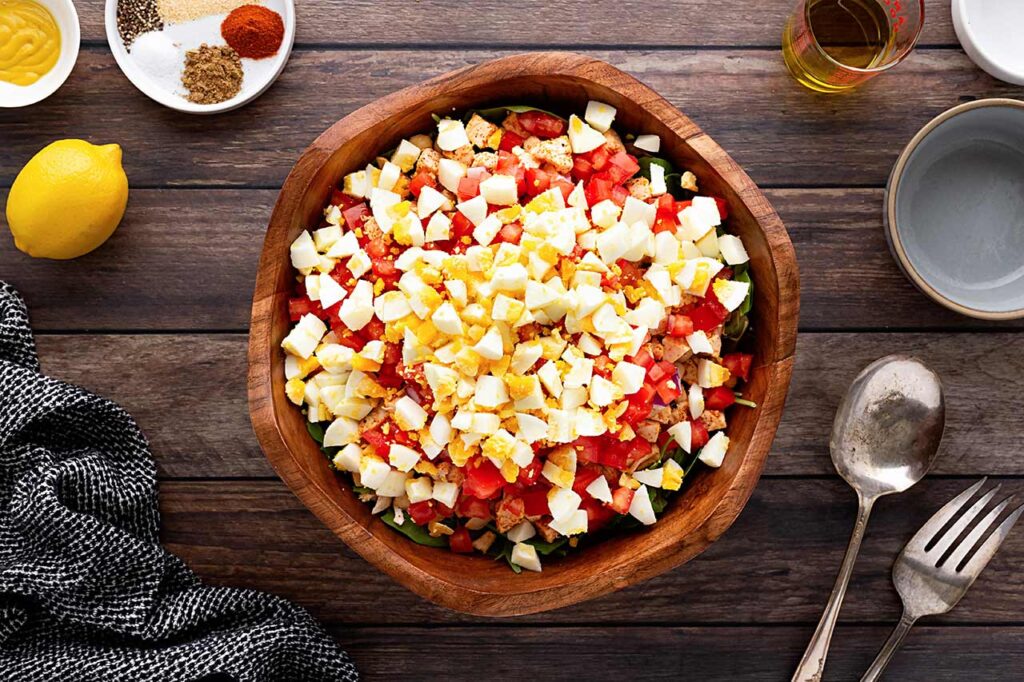 Chopped, hard-boiled egg added to salad layers in a wood bowl.