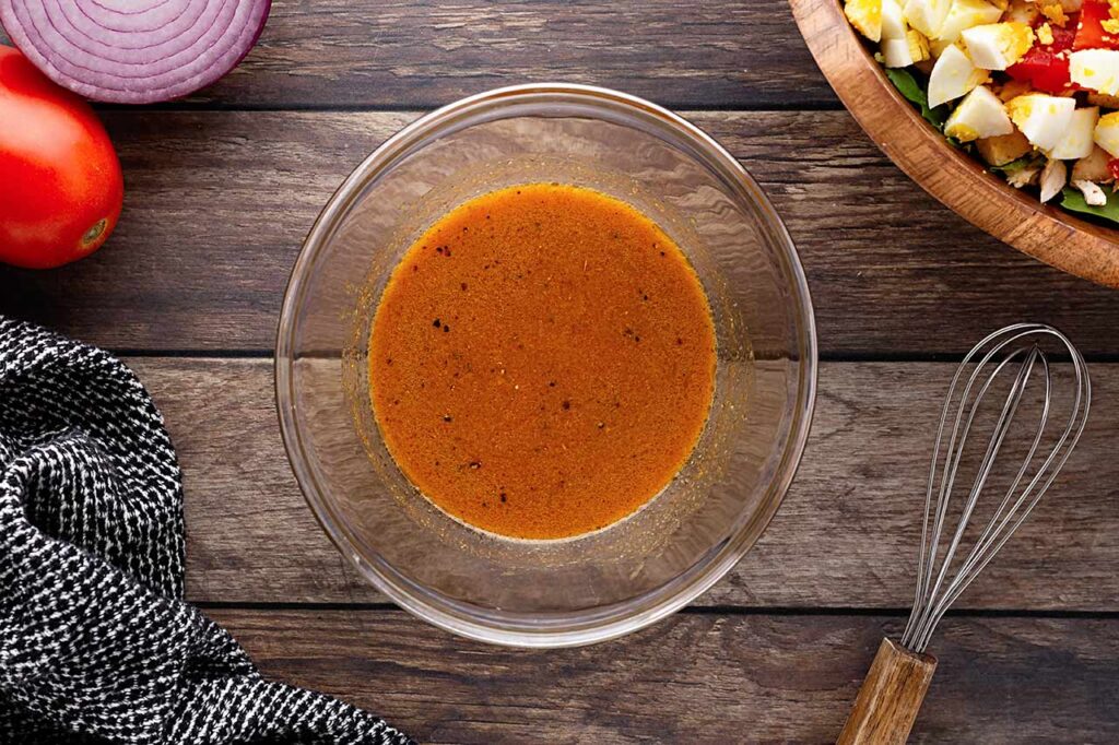 Dressing ingredients whisked together in a small, glass bowl.