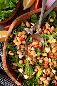 Overhead focus. High Protein Dense Bean Salad with serving utensils in a wood bowl.