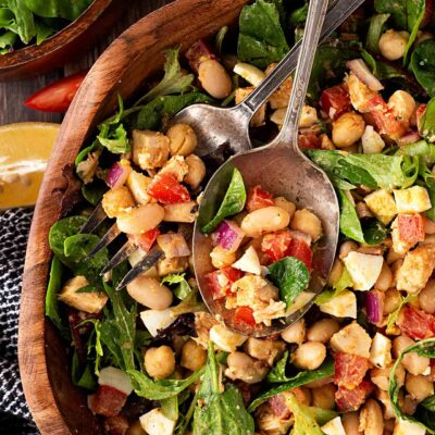 Overhead focus. High Protein Dense Bean Salad with serving utensils in a wood bowl.
