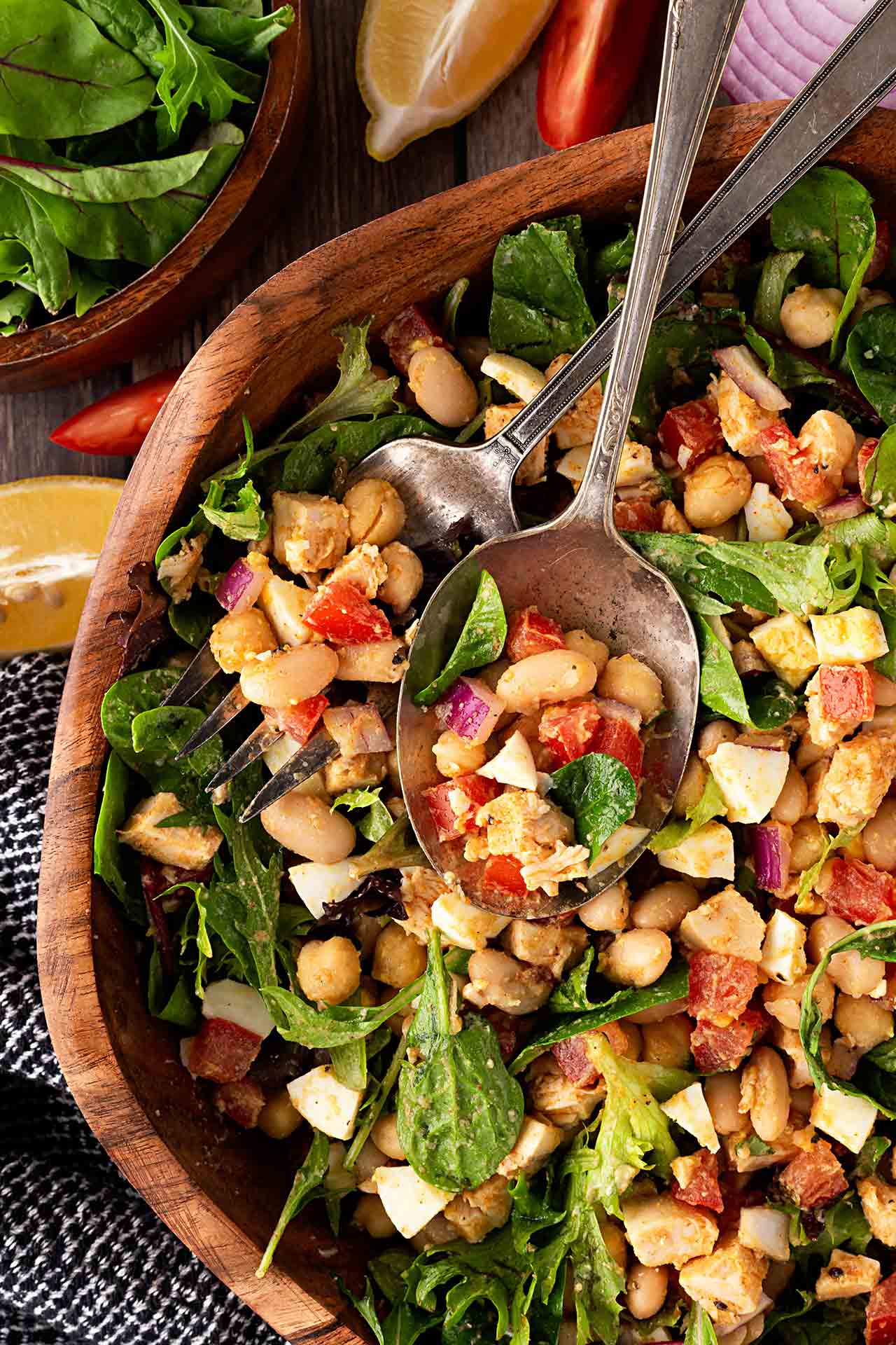 Overhead focus. High Protein Dense Bean Salad with serving utensils in a wood bowl.